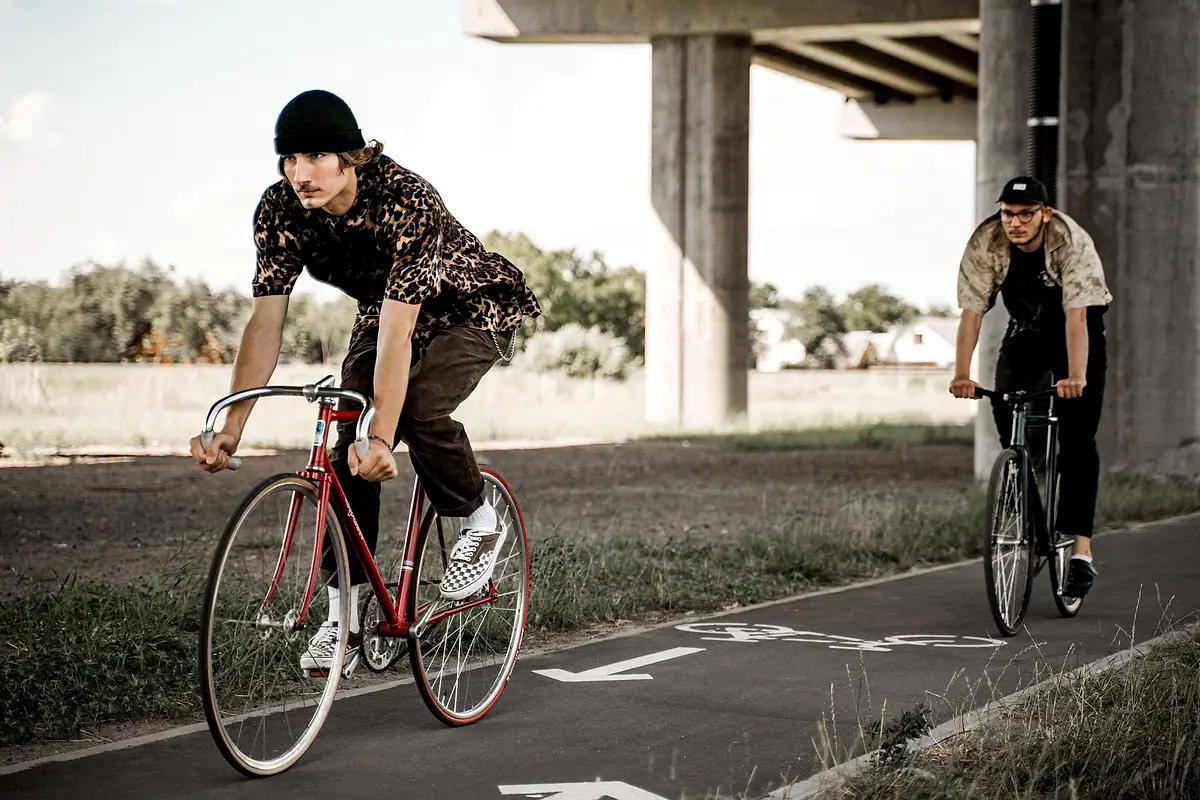 Two cyclists riding in a marked bike lane beneath an overpass.