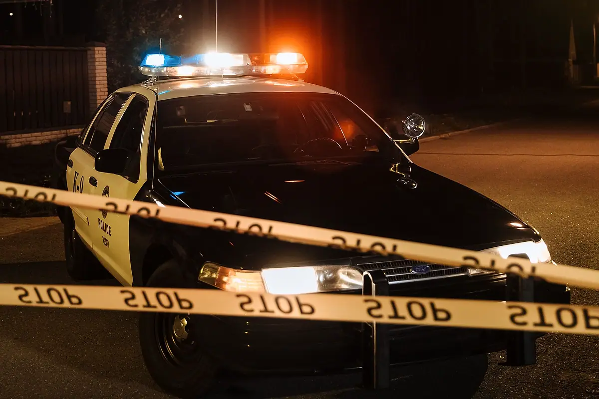 A police car with flashing lights behind a line of police tape at night.