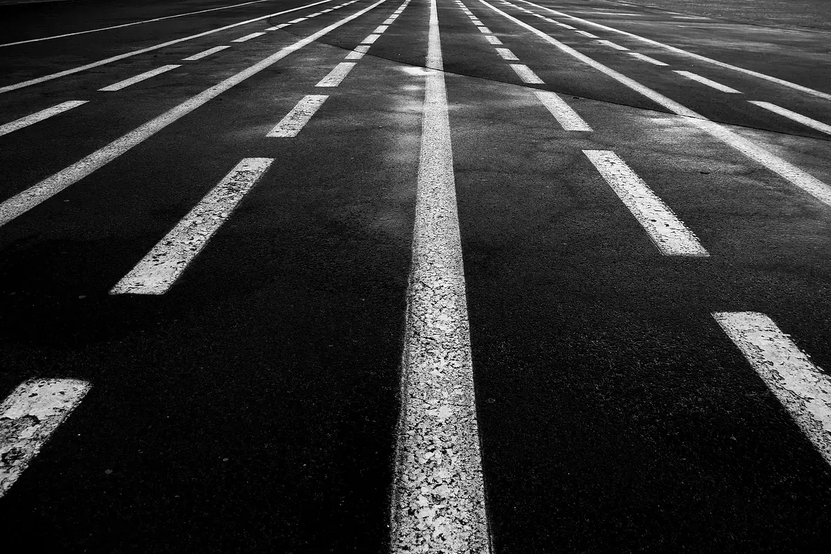 Black-and-white close view of painted lane lines on wet asphalt.