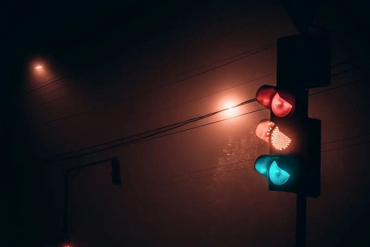 A traffic signal glowing red and green in fog at night.