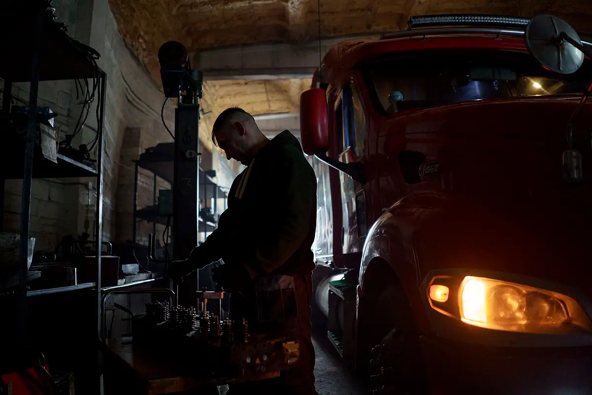 A mechanic working at a bench beside a red truck in a dim repair shop.
