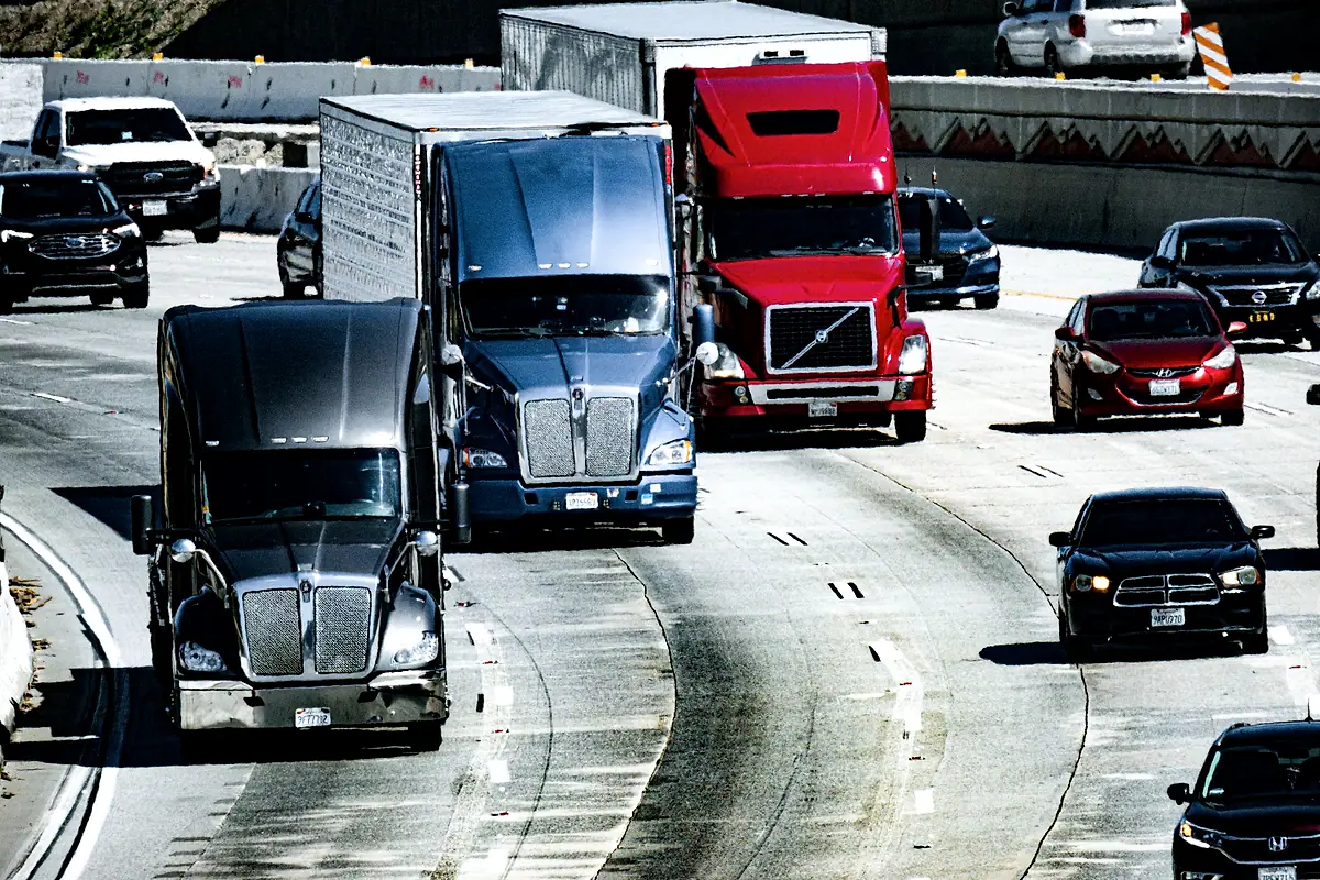 Tractor-trailers and passenger cars in heavy traffic on a curving multilane highway.